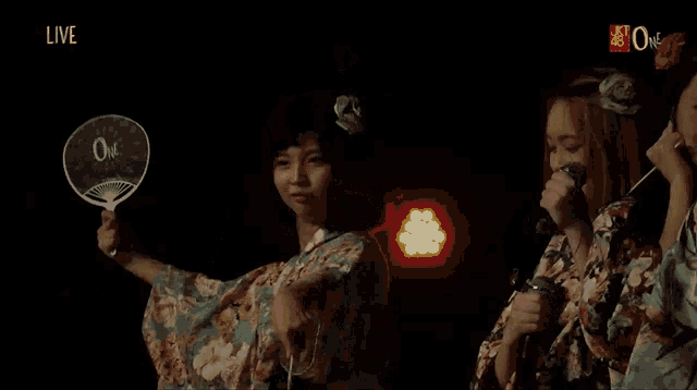 a woman in a kimono holds a fan and a red light while another woman looks on