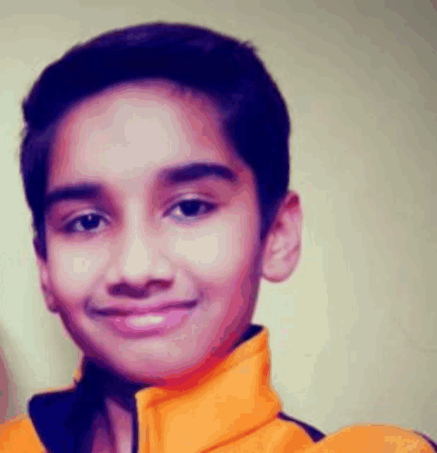 a young boy in an orange jacket smiles for the camera