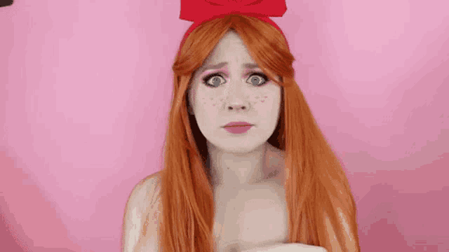 a woman with red hair and freckles is wearing a red bow on her head and making a sad face .