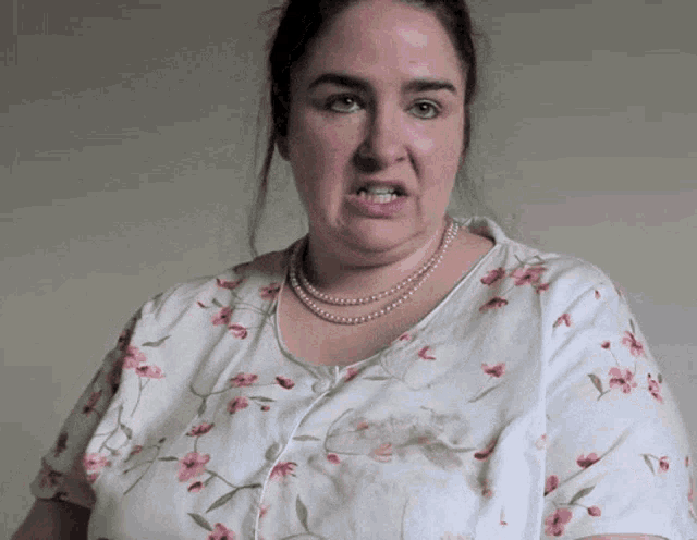 a woman wearing a floral shirt and pearls looks angry