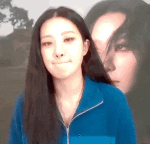 a woman in a blue jacket is making a face in front of a blurry picture of another woman .