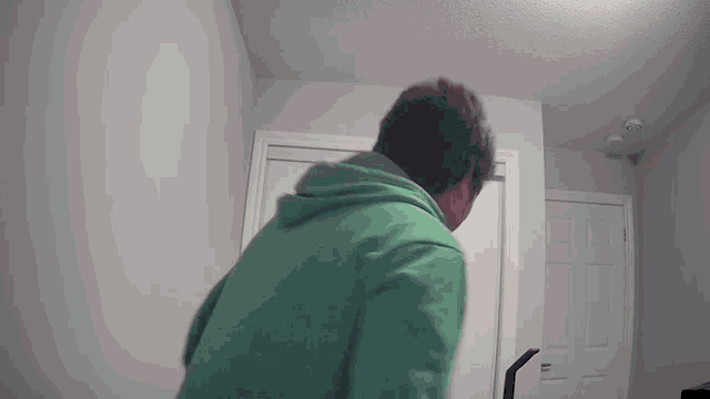 a man in a green hoodie is standing in a room