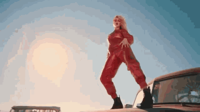 a woman in a red jumpsuit is standing on a car hood .