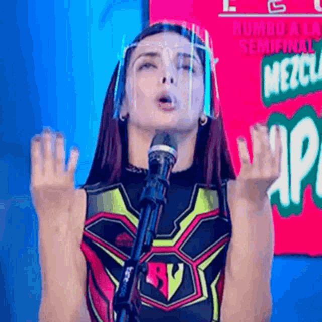 a woman wearing a face shield is standing in front of a microphone .