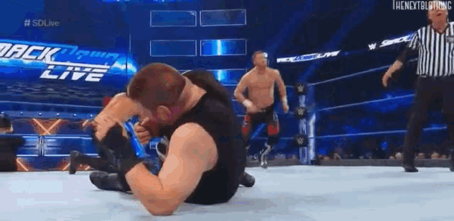 a man is laying on the ground in a wrestling ring with a referee standing behind him .