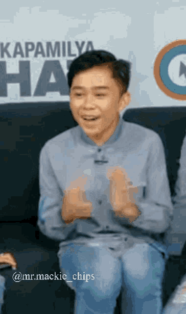 a young boy is sitting on a couch with his hands in the air and smiling .
