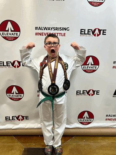 a boy stands in front of an elevate martial arts banner