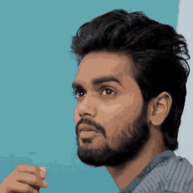 a man with a beard looks to the side with a blue background
