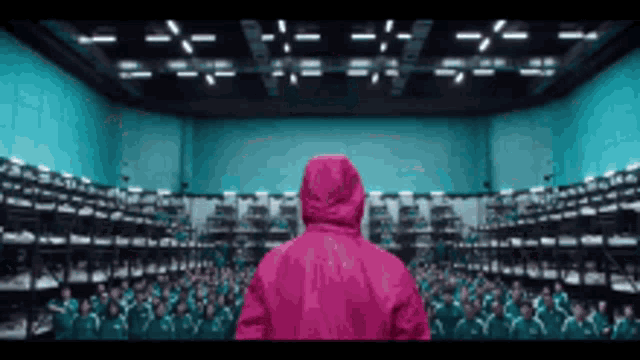a man in a pink jacket is standing in front of a large group of people in a room .