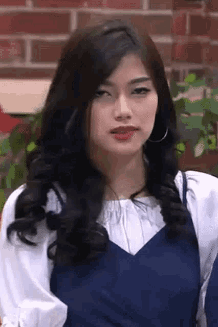 a woman with long black hair and hoop earrings is wearing a blue dress and a white shirt .