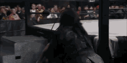 a wrestler is standing in front of a crowd in a wrestling ring .