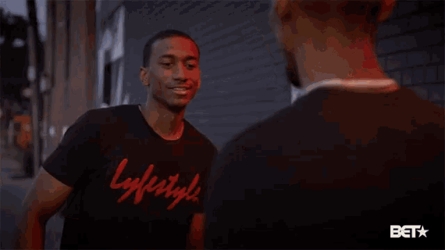 a man wearing a lifestyle t-shirt smiles while talking to another man