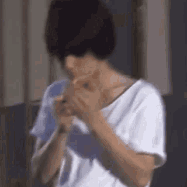 a man in a white shirt is smoking a cigarette while standing in front of a window .