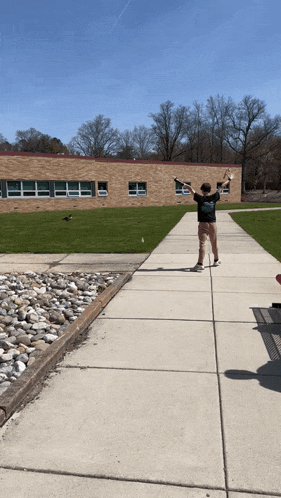 a person standing on a sidewalk in front of a building with their arms in the air
