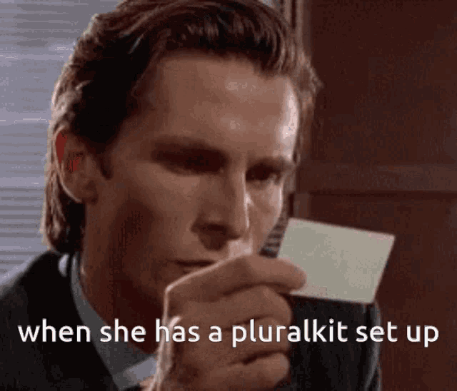 a man in a suit is holding a card in his hand and says " when she has a pluralkit set up "