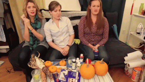 three women sit on a couch in front of a table with pumpkins and a box of toothpaste
