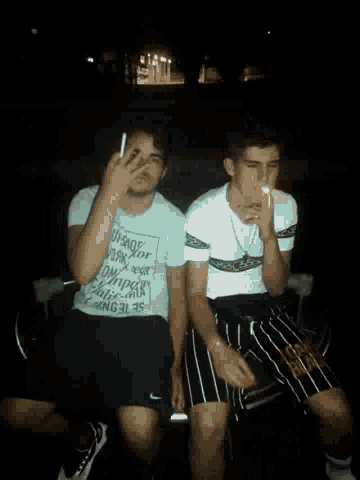 a man smoking a cigarette next to another man wearing a t-shirt that says " dangerous "