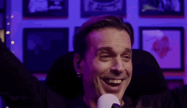 a man is laughing in front of a microphone with a hot sign in the corner .