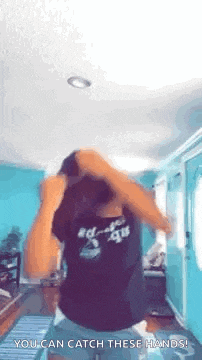 a woman in a black shirt is dancing in a living room with her hands in her hair .