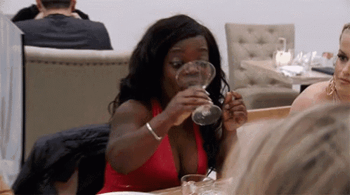 a woman in a red dress is drinking from a glass while sitting at a table in a restaurant .