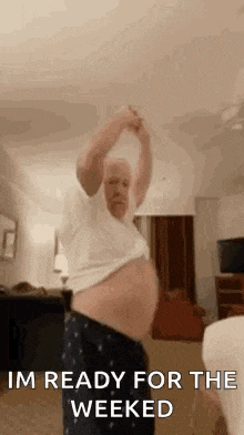 an older man is dancing in a living room with his shirt off and his belly visible .