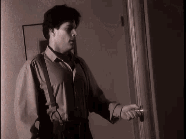 a man in suspenders is opening a door in a black and white photo