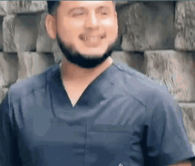 a man with a beard wearing a blue scrub top is smiling .