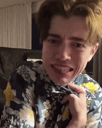a young man wearing a floral shirt is making a funny face while sitting on a couch .