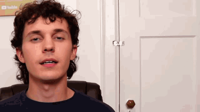 a man sitting in front of a door with a youtube sign on the wall behind him