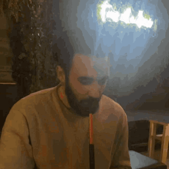 a man with a beard is smoking a hookah in front of a sign that says ' shisha '
