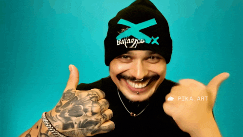 a man wearing a black beanie with a blue x on it is smiling and giving a thumbs up