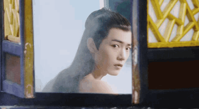 a man with long hair looks out a window