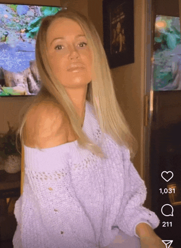 a woman wearing a purple off the shoulder sweater stands in front of a tv