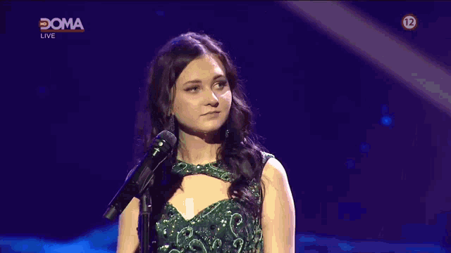 a woman in a green dress stands in front of a microphone with a sign that says doma live