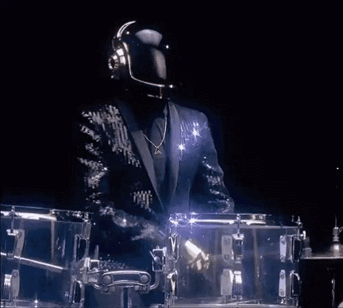 a man in a suit and helmet is playing a drum set in a dark room .