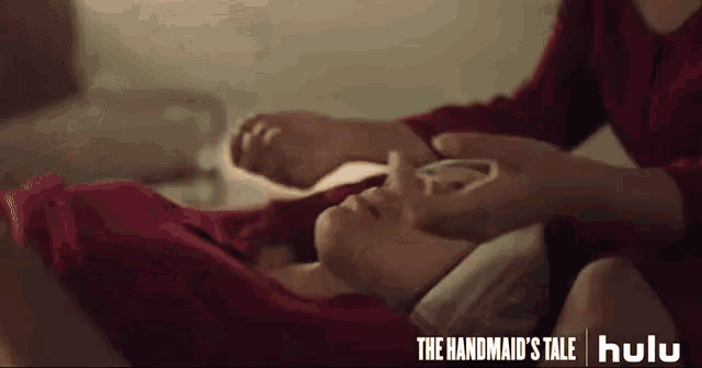 a woman in a red sweater is laying on a bed holding a child 's head .
