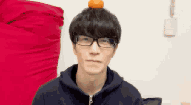 a man with glasses and an orange on his head is making a funny face .