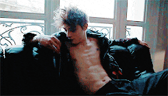 a shirtless man is laying on a black leather couch in front of a window