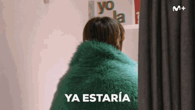 a woman in a green fur coat is standing in front of a sign that says yo la
