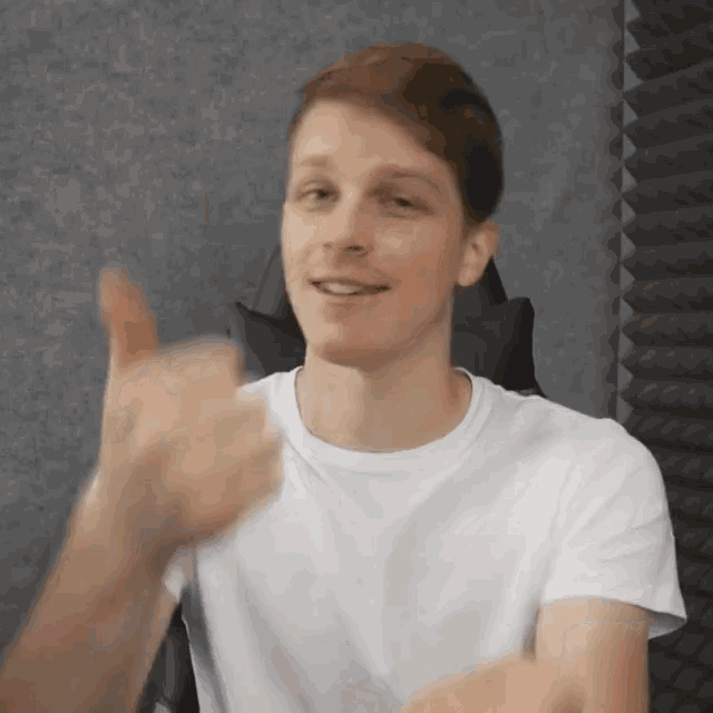 a man in a white t-shirt is giving a thumbs up sign .