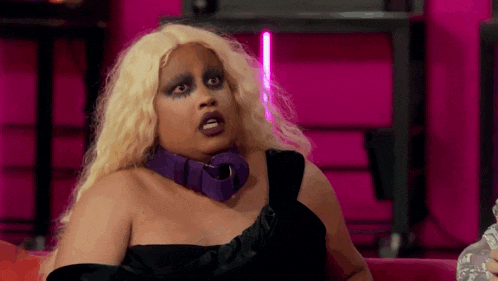 a drag queen is sitting on a couch wearing a purple choker and a black dress .