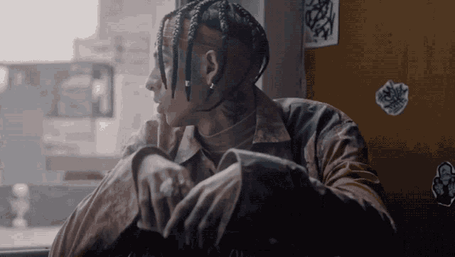 a man with dreadlocks and a tattoo on his neck looks out of a window
