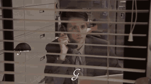 a man in a suit and tie is talking on a phone and the letter g is visible behind him