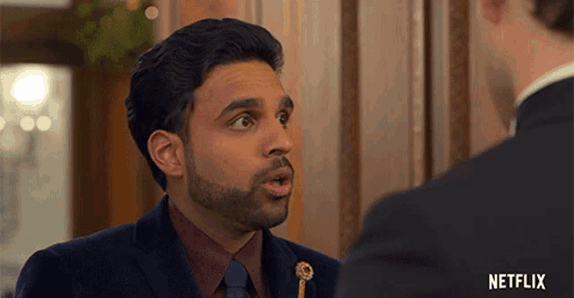 a man in a suit and tie talking to another man with a netflix logo on the bottom right