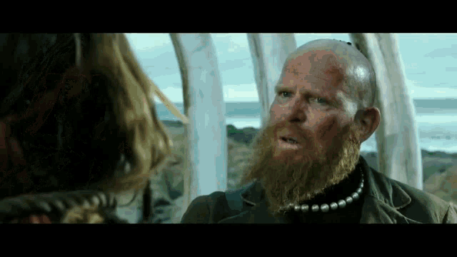 a man with a beard wearing a pearl necklace is talking to a woman