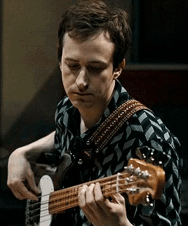 a man in a plaid shirt is playing a guitar with a red strap