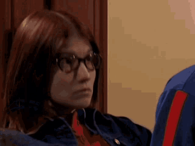 a woman wearing glasses and a blue jacket is looking at a man .