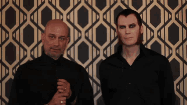 two men standing in front of a patterned wallpaper