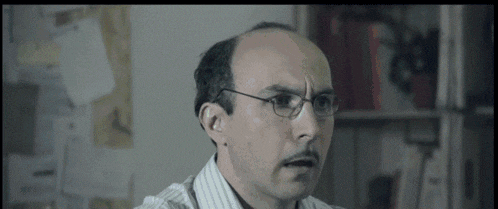 a man wearing glasses and a striped shirt looks surprised