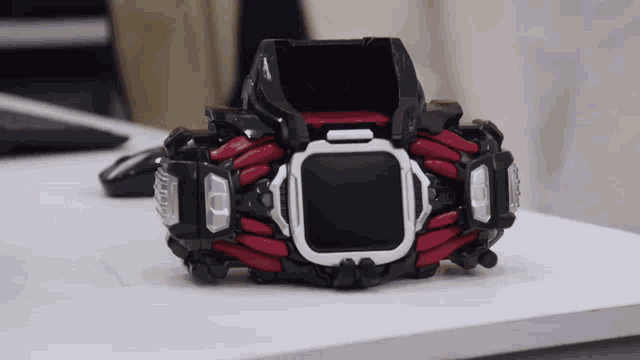 a black and red device that looks like an apple watch sits on a white table